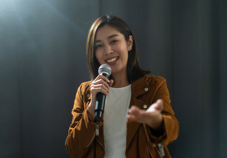 Attractive singer woman singing music on stage with spotlight strike through the darkness at concert event. Musician performing live with light in hall.の写真素材
