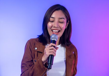Attractive singer woman singing music on stage with spotlight strike through the darkness at concert event. Musician performing live with neon light in hall.の写真素材