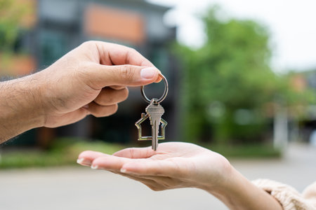 Woman buying or rent new home she holding key front of new house. Surprise happy young asian woman giving house key and smile to rent or purchase apartment home. Moving relocation concept.の写真素材