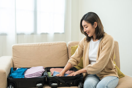 Happy Beautiful woman to folding her clothes pack suitcase for travel in holiday. Young female folding clothes while packing luggage at home.の写真素材
