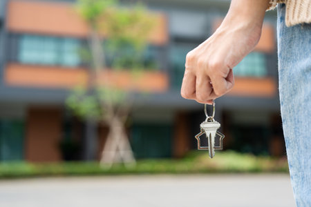 Woman buying or rent new home she holding key front of new house. Surprise happy young asian woman giving house key and smile to rent or purchase apartment home. Moving relocation concept.の写真素材