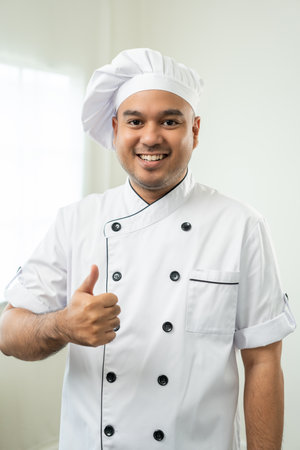 Vertical of Smiling Young handsome asian man chef in uniform with hat standing posting looking at...