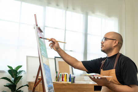 Asian man artist working on painting with brush and variant acrylic color. Man artist painter on canvas in creative studio as art conceptの写真素材