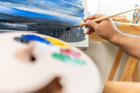 Asian man artist working on painting with brush and variant acrylic color. Man artist painter on canvas in creative studio as art conceptの写真素材