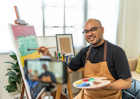 Asian man artist working on painting record video broadcasting live teaching how to brush and variant acrylic color in classroom online. Man artist painter on canvas in creative studio as art conceptの写真素材