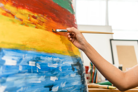 Close up hand Asian woman artist working on painting with brush and variant acrylic color. Female artist painter on canvas in creative studio as art conceptの写真素材