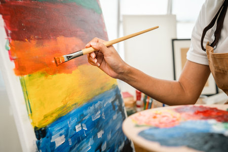Close up hand Asian woman artist working on painting with brush and variant acrylic color. Female artist painter on canvas in creative studio as art conceptの写真素材
