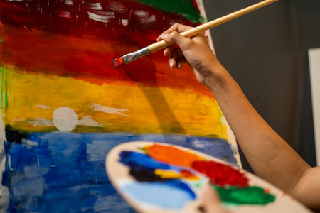 Close up woman hand artist in the darkroom warm light working on painting with brush and variant acrylic color. Female artist painter on canvas in creative studio as art conceptの写真素材