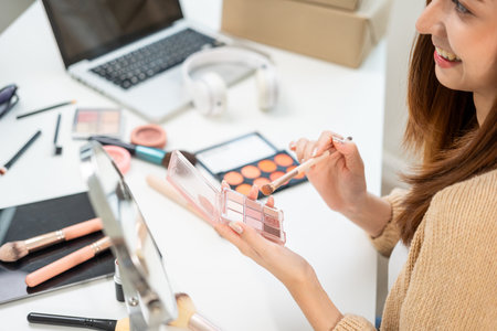 Young beautiful asian woman vlogger live broadcasting cosmetic makeup tutorial content with eye shadow. Influencers professional beauty make up with various cosmetics recording video on social mediaの写真素材