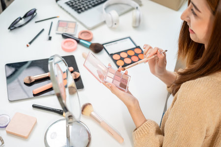 Young beautiful asian woman vlogger live broadcasting cosmetic makeup tutorial content with eye shadow. Influencers professional beauty make up with various cosmetics recording video on social mediaの写真素材