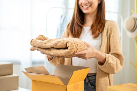 Woman business owner at fashion store packing clothing in the parcel cardboard box and delivery to customer. Asian female entrepreneur working in clothes shop.の写真素材