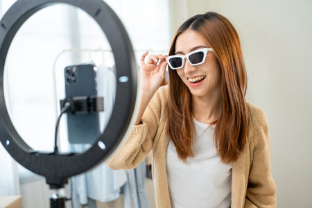 Young asian woman business owner at fashion store using cellphone live streaming for sale fashion...