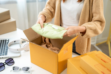 Woman business owner at fashion store packing clothing in the parcel cardboard box and delivery to customer. Asian female entrepreneur working in clothes shop.の写真素材