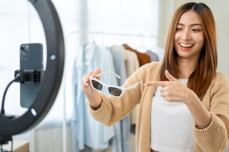 Young asian woman business owner at fashion store using cellphone live streaming for sale fashion sunglasses. Influencers record video review item for sell on social media. Online shoppingの写真素材