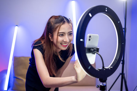 Young trendy influencer asian woman dancing on mobile phone at home in living room with neon light....