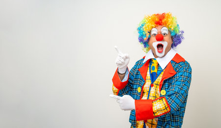 Mr Clown. Portrait of Funny comedian face Clown man in colorful uniform pointing finger to copy space for text advertise. Happy expression amazed male bozo in various pose on isolated background.の写真素材