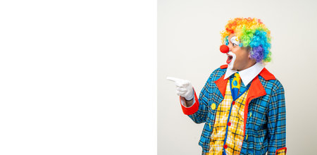 Mr Clown. Portrait of Funny comedian face Clown man in colorful uniform pointing finger to copy space for text advertise. Happy expression amazed male bozo in various pose on isolated background.の写真素材
