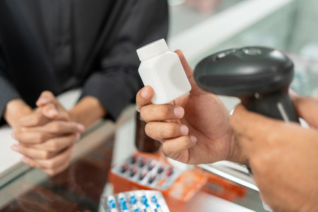 Payment with Barcode scanning to sell medicines. Pharmacist recommends medicines to customers. Professional Asian male pharmacist selling medications to female patient at drugstore shelves.の写真素材