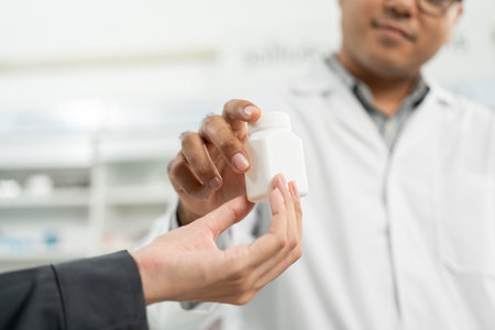 Pharmacist recommends medicines to customers. Asking the questions of medication. Professional Asian male pharmacist giving prescription medications to female patient customers at drugstore shelves.の写真素材