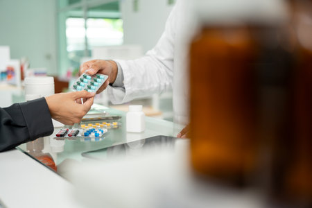 Pharmacist recommends medicines to customers. Asking the questions of medication. Professional Asian male pharmacist giving prescription medications to female patient customers at drugstore shelves.の写真素材
