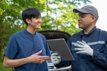 Professional mechanic talking in a conversation with the car owner, explaining the car's issue and the methods of repair. Checking the broken engine and damage as listed. Repair car outside service.の写真素材