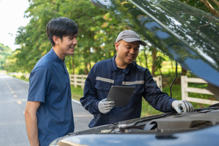 Professional mechanic talking in a conversation with the car owner, explaining the car's issue and the methods of repair. Checking the broken engine and damage as listed. Repair car outside service.の写真素材