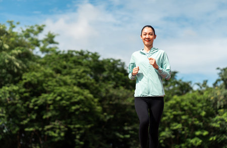 Happy asian slim woman wearing sportswear jogging on track at sport stadium. Young beautiful asian female in sports bra running outdoor. Workout exercise in the morning. Healthy and active lifestyleの写真素材