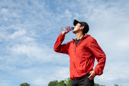 Handsome indian man drinking water after workout exercising in the stadium. Young asian man drinking water after jogging running outdoor at running track. Healthy and active lifestyle concept.の写真素材