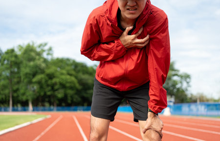Young asian indian man tired during jogging on the track in sport stadium. Young asian male intense training workout challenge breathing exhausted. Healthy and active lifestyle concept.の写真素材