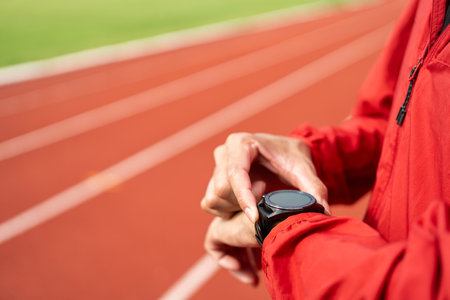 Young man wearing sportswear red jacket using Smart Watch Showing Heart Rate Monitor. Technology for health and sport mode. Exercise and take statistics to develop your potential at sport stadiumの写真素材