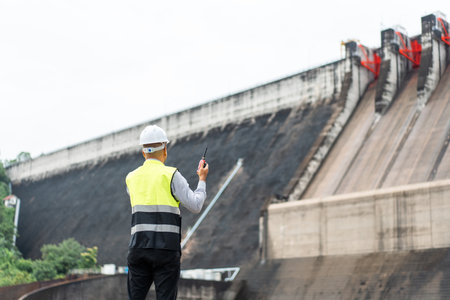 Professional asian maintenance engineer man with safety helmet in construction site dam with hydroelectric power plant and irrigation. Manager engineer man working at project big building.の写真素材