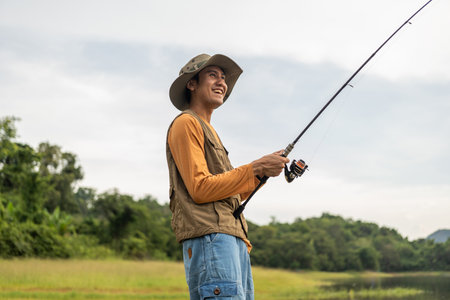 Enjoy moment of Handsome man fishing as a leisure activity during his vacation at the lake on sunset. Silhouette at sunset moment of man fishing rotation with reel.の写真素材