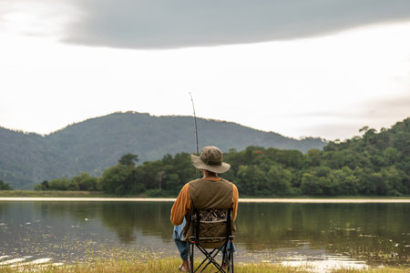 Enjoy moment of Handsome man fishing as a leisure activity during his vacation at the lake on sunset. Silhouette at sunset moment of man fishing rotation with reel.の写真素材