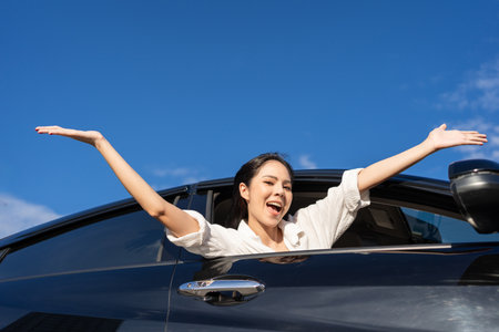 Young beautiful asian business women getting new car. Happy smiling female driving vehicle on the road Sticking her head outta the windshield with sun light. Business woman buying driving new carの写真素材