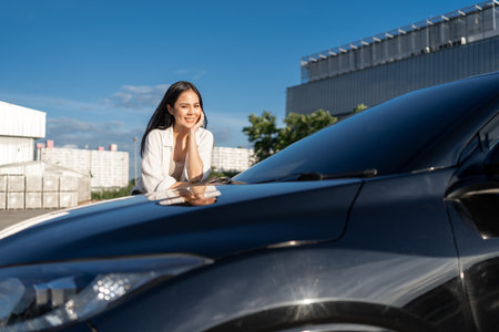 Young beautiful asian women buying new car. she was standing near car on the roadside. Beautiful moment blue sky Smiling female driving travel by vehicle on the road on a bright day with sun light.の写真素材
