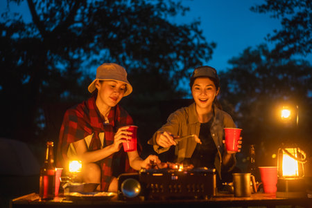 Cheers! Group of asian people friend party camping in nature making toasting with soft drink and beer red cup. Hangout party outdoor in campsite nature forest background on holiday weekend vacationの写真素材