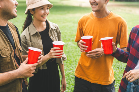 Cheers! Group of asian people friend party camping in nature making toasting with soft drink and beer red cup. Hangout party outdoor in campsite nature forest background on holiday weekend vacationの写真素材