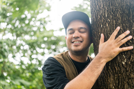 Young asian man traveller relaxing in nature forest background. Happy male hugging big tree....