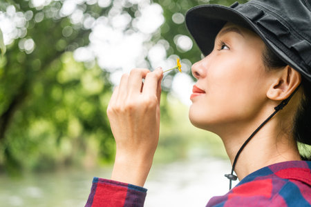 Young asian woman traveller relaxing in nature forest background. Happy woman holding little flower...