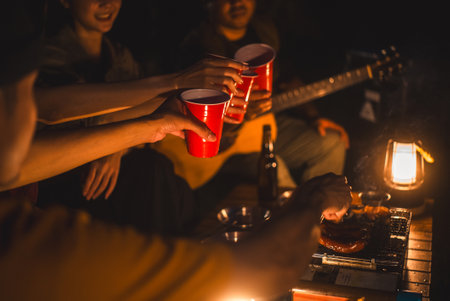 Cheers! Group of asian people friend party camping in nature making toasting with soft drink and beer red cup. Hangout party outdoor in campsite nature forest background on holiday weekend vacationの写真素材