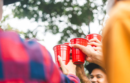 Cheers! Group of asian people friend party camping in nature making toasting with soft drink and beer red cup. Hangout party outdoor in campsite nature forest background on holiday weekend vacationの写真素材