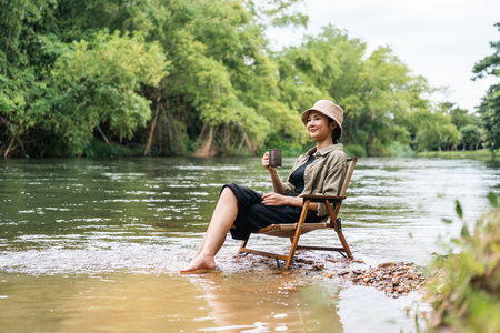 Young asian woman traveller drinking coffee in nature forest background. Happy Beautiful woman living middle of a lot of tree. Breathing the fresh air on her vacation weekend holiday trip.の写真素材