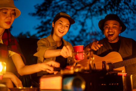 Cheers! Group of asian people friend party camping in nature making toasting with soft drink and beer red cup. Hangout party outdoor in campsite nature forest background on holiday weekend vacationの写真素材