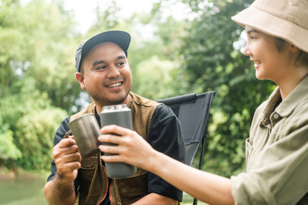 Young asian couple man and woman drinking coffee sitting in campsite outdoor. Two people camping in...