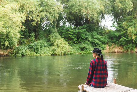 Young asian woman traveller relaxing in nature forest and river background. Happy Beautiful woman living in middle of a lot of tree. Breathing the fresh air on her vacation weekend holiday trip.の写真素材