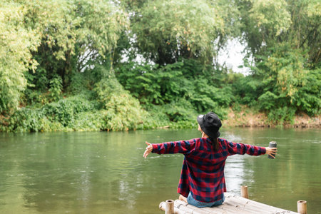Young asian woman traveller relaxing in nature forest and river background. Happy Beautiful woman living in middle of a lot of tree. Breathing the fresh air on her vacation weekend holiday trip.の写真素材