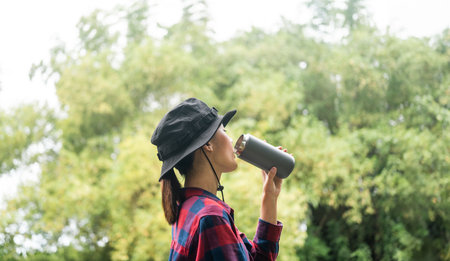 Young asian woman traveller drinking coffee standing in nature forest background. Happy Beautiful...