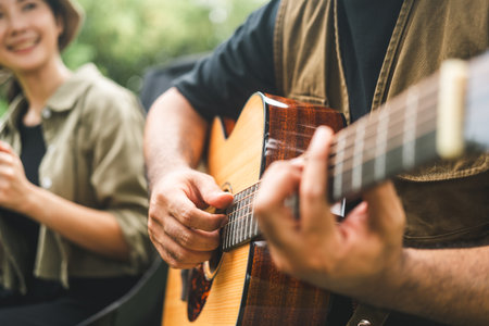 Young asian couple man and woman picnic sitting in campsite outdoor garden. Two people camping in forest playing guitar and drinking coffee. Travel relax camping on vacation holiday weekend themeの写真素材