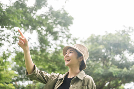 Young asian woman traveller relaxing in nature forest background. Happy Beautiful woman standing middle of a lot of tree. Breathing the fresh air on her vacation weekend holiday trip.の写真素材