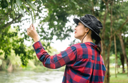 Young asian woman traveller relaxing in nature forest background. Happy woman holding little flower and smell. Breathing the fresh air on her vacation weekend holiday trip. Human and natural.の写真素材